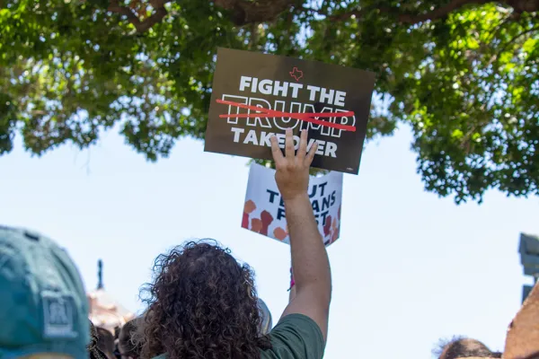 An AFSCME Local 1624 member stands in a crowd holding up a sign reading "Fight the Trump Takeover" at the 07/24 Austin rally.
