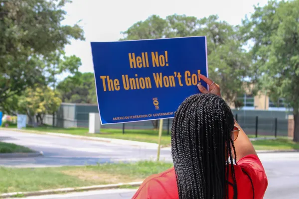 An AFGE member holds a sign reading, "Hell No! The Union Won't Go!