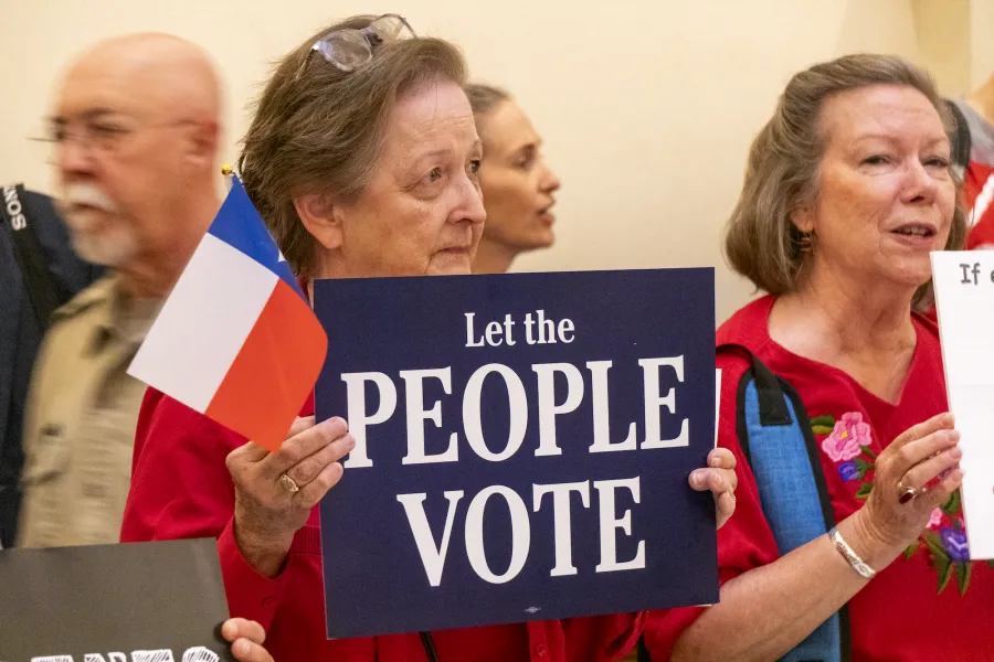 A woman holds up a Texas flag with a sign that says "Let the people vote"