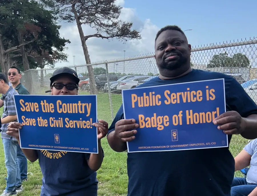 Two AFGE members hold signs in support of public service