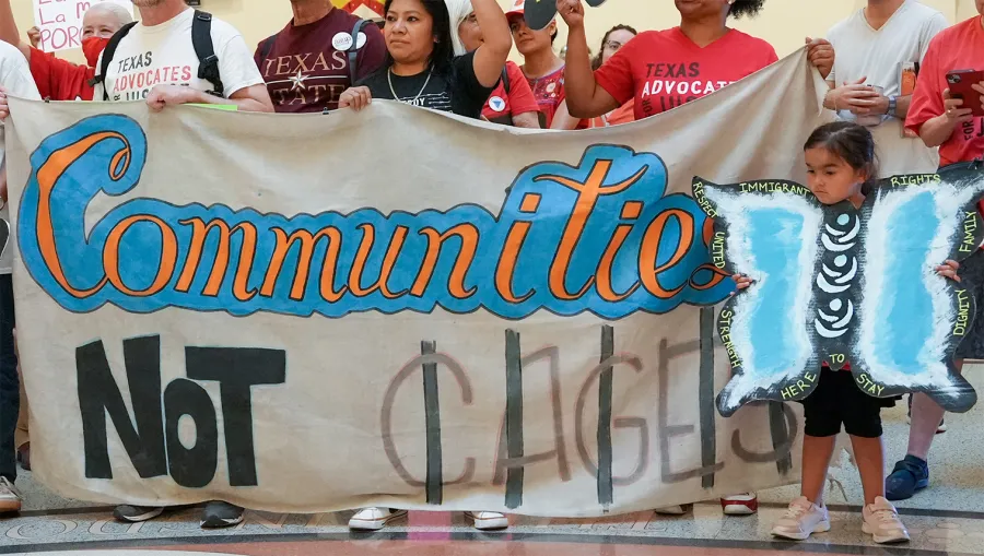 Volunteers at a Workers Defense event stand behind a banner that reads, "Communities, NOT CAGES."