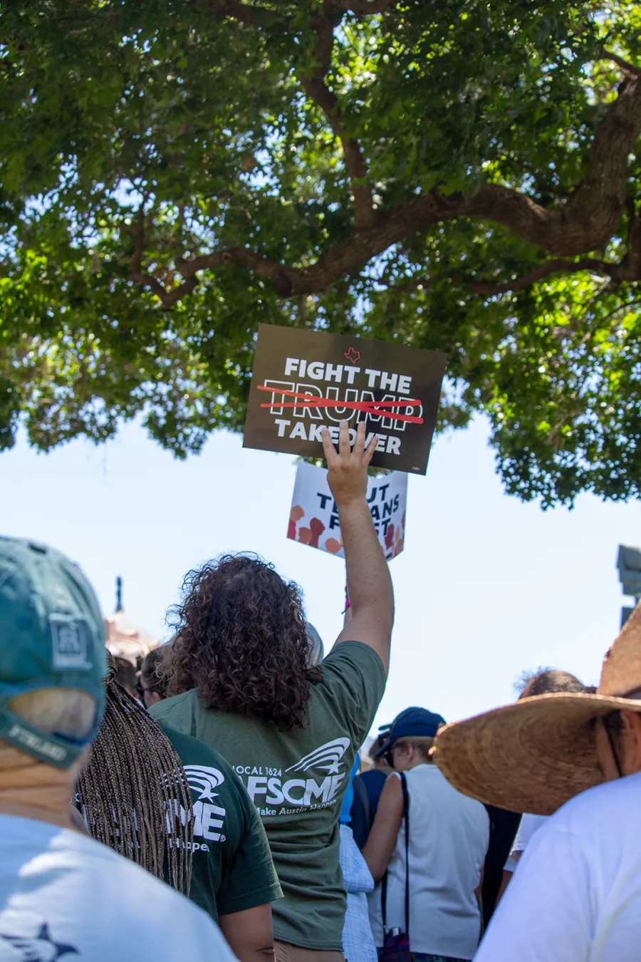 An AFSCME Local 1624 member stands in a crowd holding up a sign reading "Fight the Trump Takeover" at the 07/24 Austin rally.