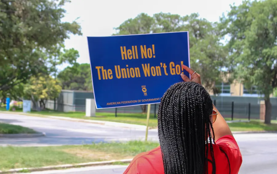 An AFGE member holds a sign reading, "Hell No! The Union Won't Go!