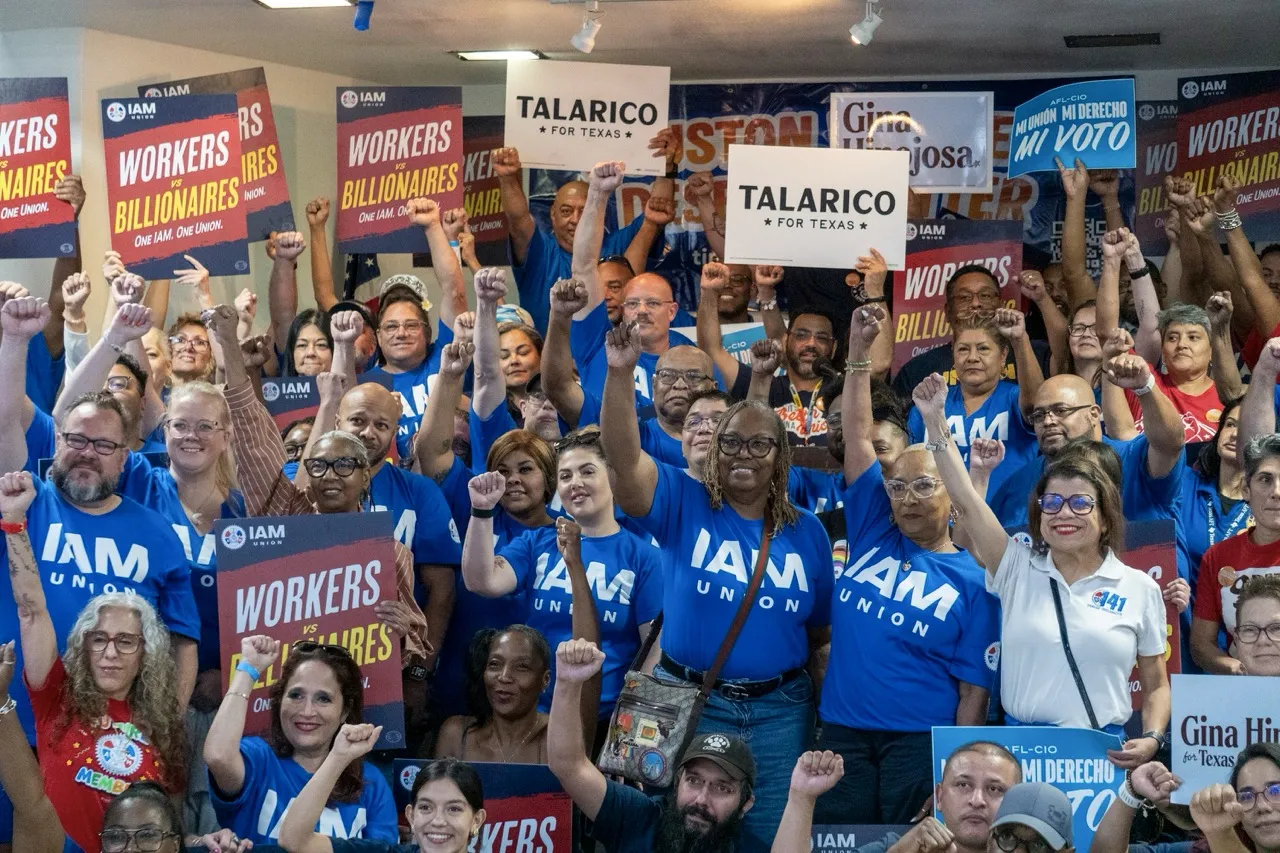 Union members stand together with their fists in the air holding Talarico and Workers vs. Billionaires signs