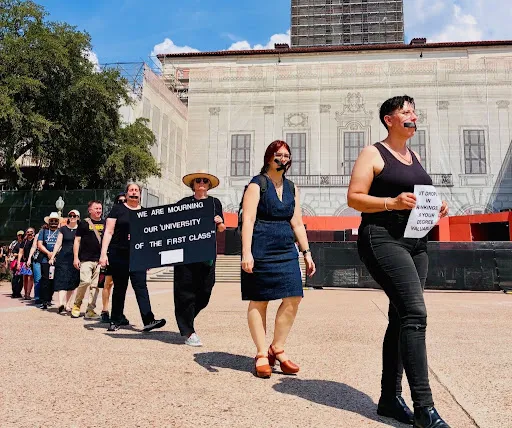 Group of AAUP at UT Austin members walk in a line, demanding academic freedom, economic security, and faculty autonomy. Protestors wear black and carry signs.